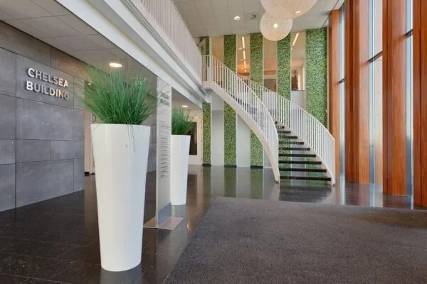 Moderne entreehal van het Chelsea Building aan de Laan van Zuid Hoorn met een witte wenteltrap, hoge plantenbakken en grote ramen.